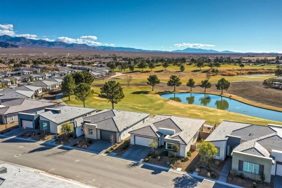 Aerial view of single-storey homes lining a fairway, with a pond and mountains in the distance