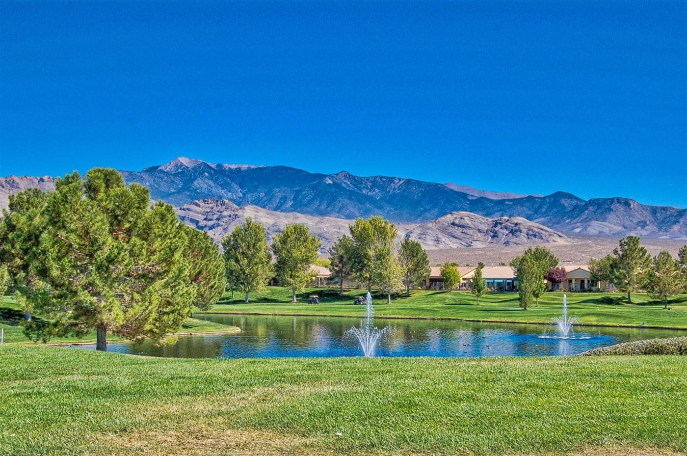 Golf course pond with fountains, framed by pines and the mountains above Pahrump
